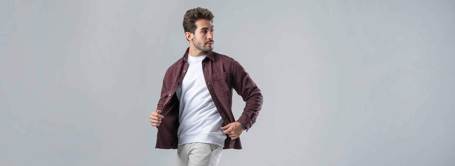 Man wearing a brown jacket over a white shirt on a gray background